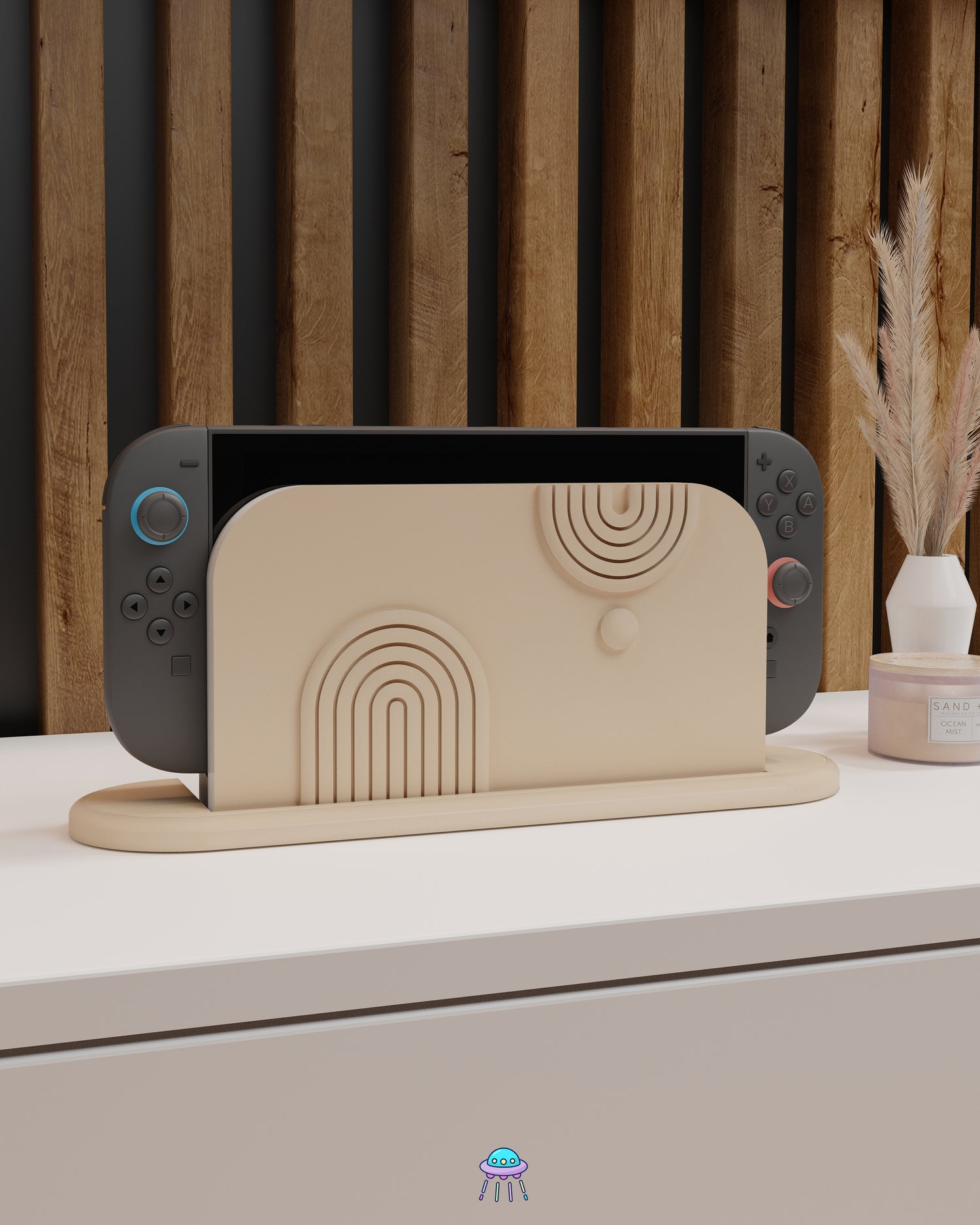 A Nintendo Switch 2 with Joy-Con controllers docked in a customised dock featuring a beige PLA filament cover and base. The cover has two embossed arch designs on the front—one larger arch at the bottom left and a smaller arch in the top right corner, alongside a small circular detail. The setup is placed on a white cabinet with a wooden panel background and decorative items nearby, including a candle and a vase with dried pampas grass.