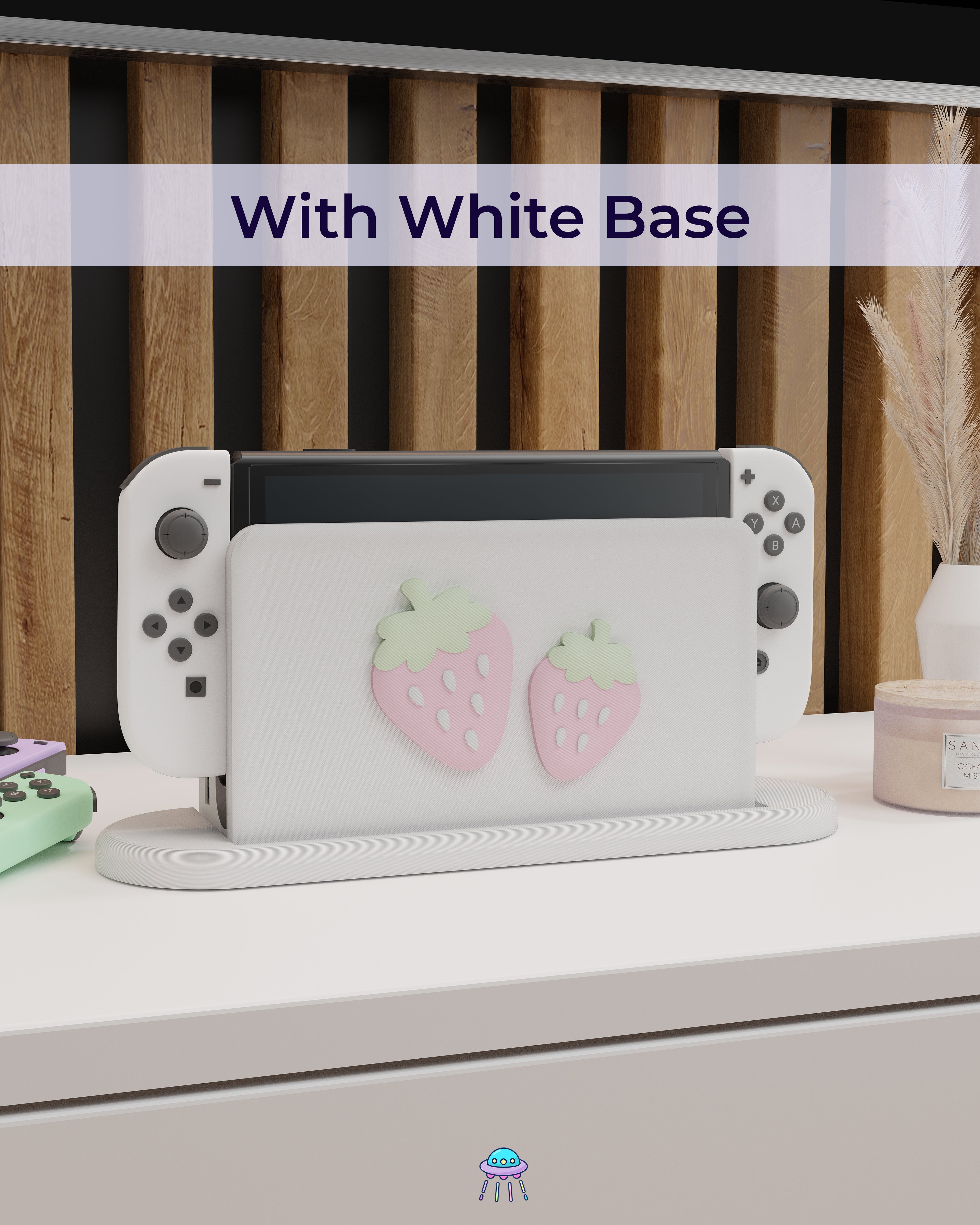 A Nintendo Switch with Joy-Con controllers docked in a customised dock featuring a white PLA filament cover and pink base. The cover has two strawberry designs on the front—one larger to the left and a smaller strawberry to the right. The setup is placed on a white cabinet with a wooden panel background and decorative items nearby, including a candle, a vase with dried pampas grass, and an additional pair of Joy-Con controllers. The title reads &