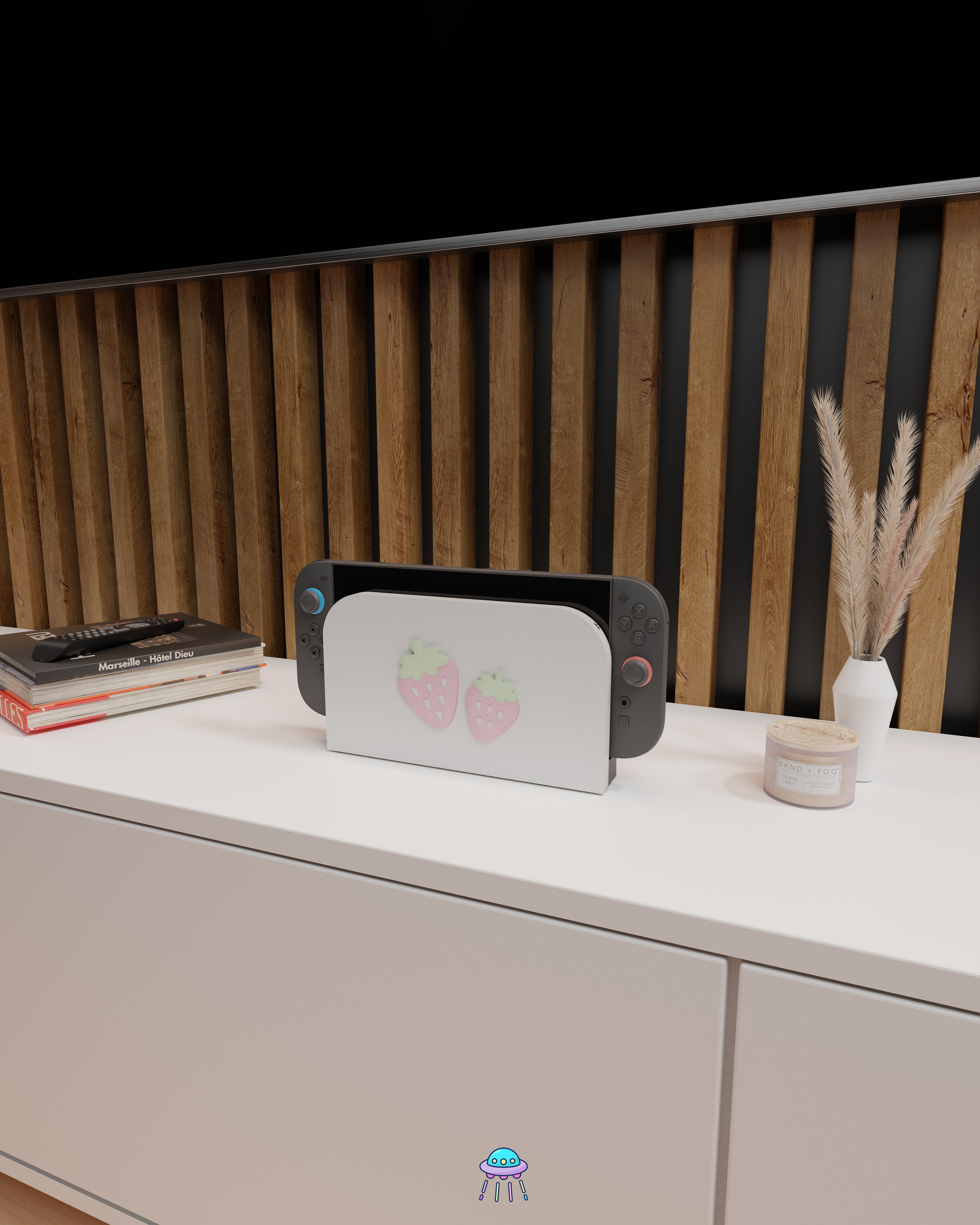 Wider angle of a Nintendo Switch 2 with Joy-Con controllers docked in a customised dock featuring a white PLA filament cover and pink base. The cover has two strawberry designs on the front—one larger to the left and a smaller strawberry to the right. The setup is placed on a white cabinet with a wooden panel background and decorative items nearby, including a candle and a vase with dried pampas grass.