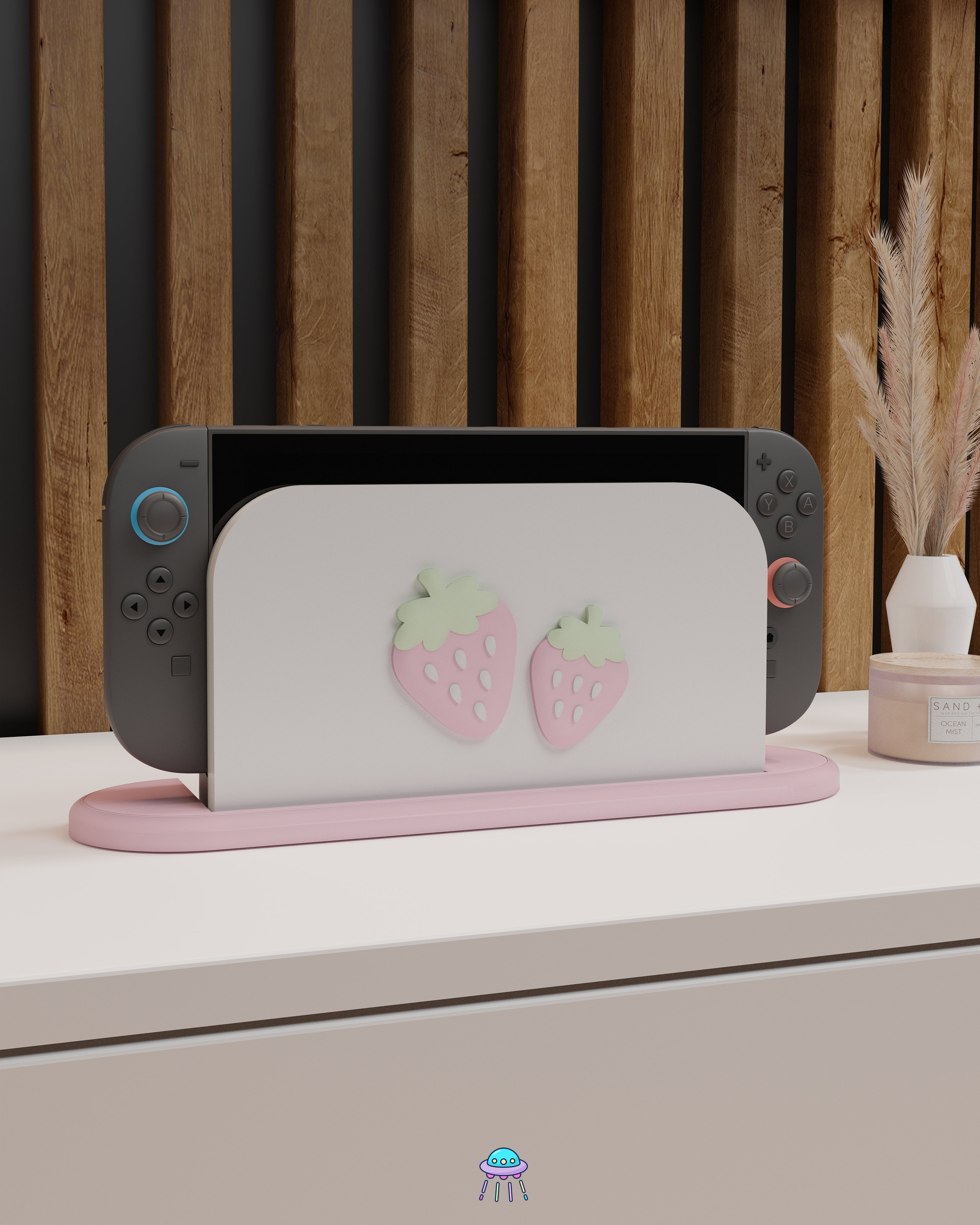A Nintendo Switch 2 with Joy-Con controllers docked in a customised dock featuring a white PLA filament cover and pink base. The cover has two strawberry designs on the front—one larger to the left and a smaller strawberry to the right. The setup is placed on a white cabinet with a wooden panel background and decorative items nearby, including a candle and a vase with dried pampas grass.