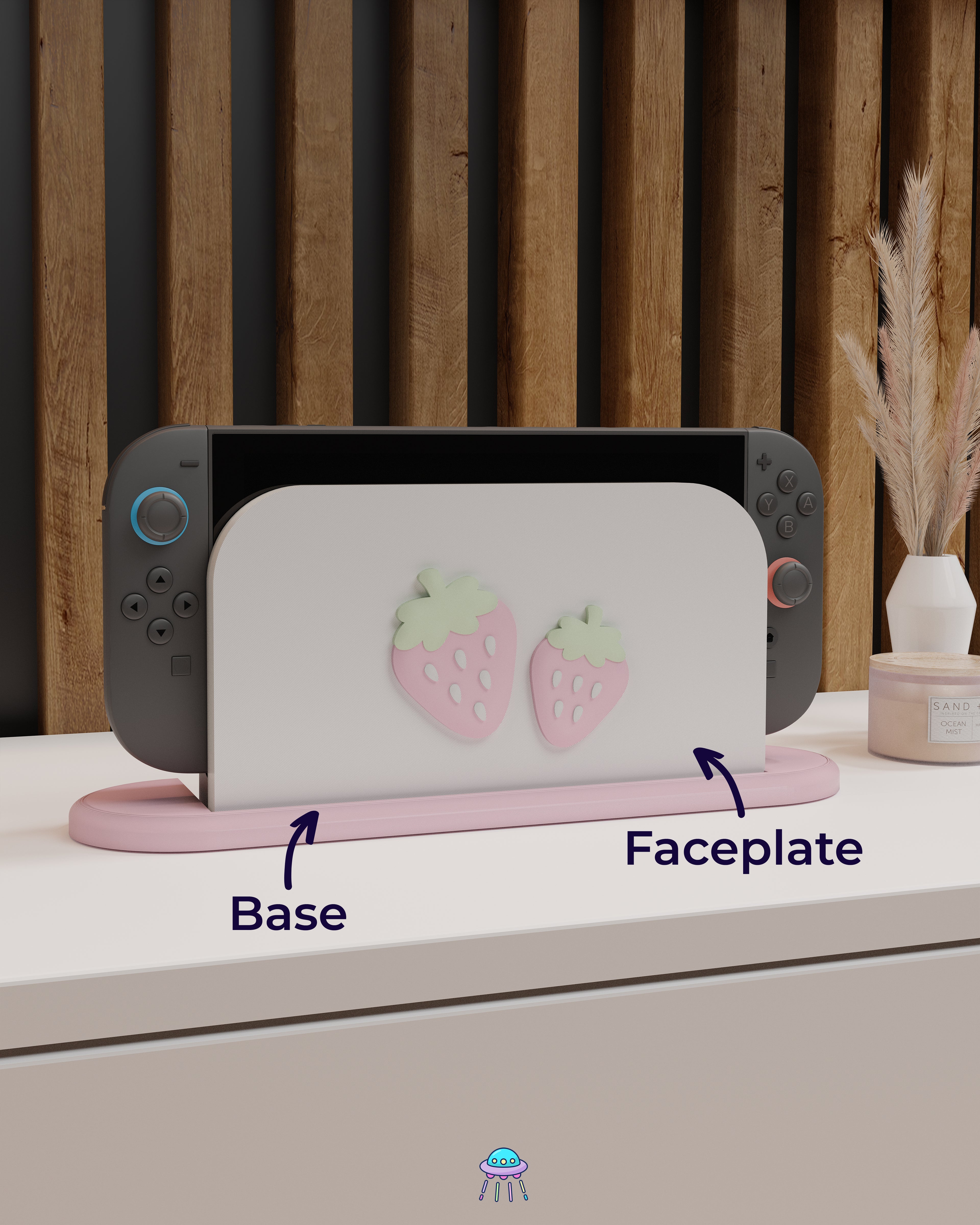 A Nintendo Switch 2 with Joy-Con controllers docked in a customised dock featuring a white PLA filament cover and pink base. The cover has two strawberry designs on the front—one larger to the left and a smaller strawberry to the right. The setup is placed on a white cabinet with a wooden panel background and decorative items nearby, including a candle and a vase with dried pampas grass. Arrows point to the faceplate and base.