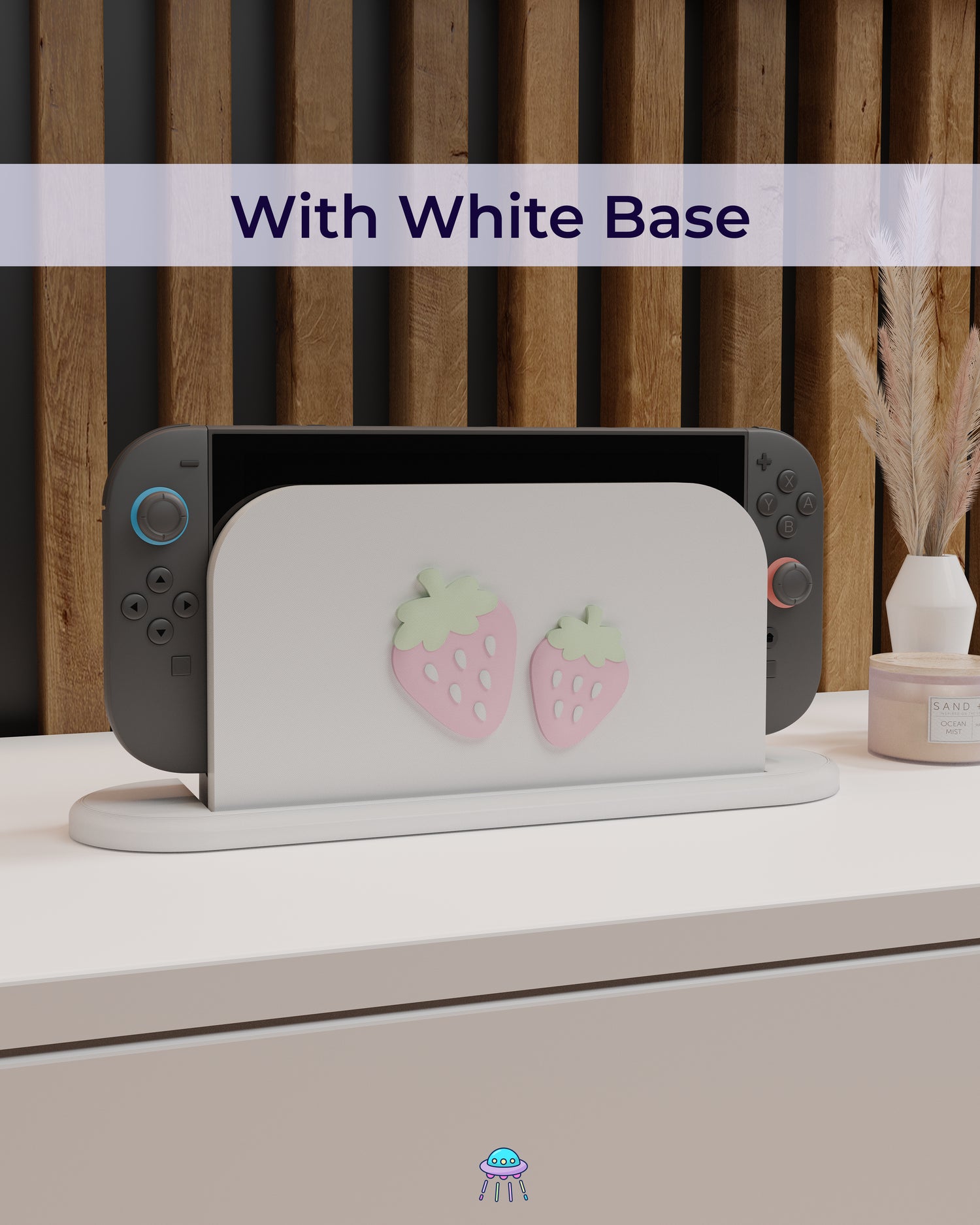A Nintendo Switch 2 with Joy-Con controllers docked in a customised dock featuring a white PLA filament cover and pink base. The cover has two strawberry designs on the front—one larger to the left and a smaller strawberry to the right. The setup is placed on a white cabinet with a wooden panel background and decorative items nearby, including a candle and a vase with dried pampas grass. The title reads &
